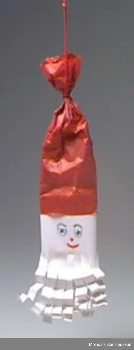 Julgranskarameller, tomtar och äpple tillverkade som pysselarbete, sannolikt på Katrinebergs daghem. MM02368:1 julgranskaramell i rött och vitt silkespapper med tomteansiktebokmärke på. Centimeterbreda veckade pappersremsor i ändarna. L: 590 mm. Diam: 50 mm.:2 Julgranskaramell i vitt och rött, som tomte med påmålat ansikte. L: 280 mm.Bredd: 60 mm.:3 Tomte av garnboll och rosa flörtkula. L: 180 mm. Diam:50 mm.:4 Tomte av rött vikt papper och bomull. L: 110 mm. Bredd: 65 mm.:5 Tomte av tallkotte, vit flörtkula och rött crépepapper. L: 150 mm.:6 Julgransäpple av röd flörtkula. L: 50 mm.:7 Hjärta av flätat halmband. L: 140 mm. B: 70 mm.Gåva av Katrinebergs Daghem genom Birgitta Bilting.