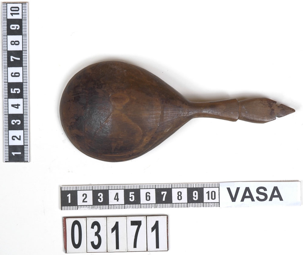 En träsked.
Skeden har ett ovalt skedblad och ett kort skaft. Skaftet är profilerat i tre avsatser. Skaftets ände är formad till en spets. På skeden syns spår av färg.
Skeden är mycket välbevarad, bortsett från en liten spricka som är synlig på baksidan.

Text in English: Wooden spoon with egg-shaped bowl and short, profiled handle ending in a point.
Intact and well preserved except for a small crack on the reverse.