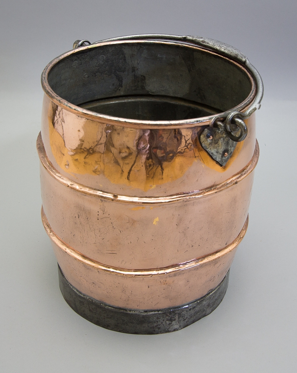 Hink av koppar och järn. Med bukig form med rullad överkant och två drivna profiler på buken. Med smidd tvärgrepe av järn fäst vid två hjärtformade fästen av järn, nitade med kopparnitar. På ett lött band av järn. Invändigt förtent.