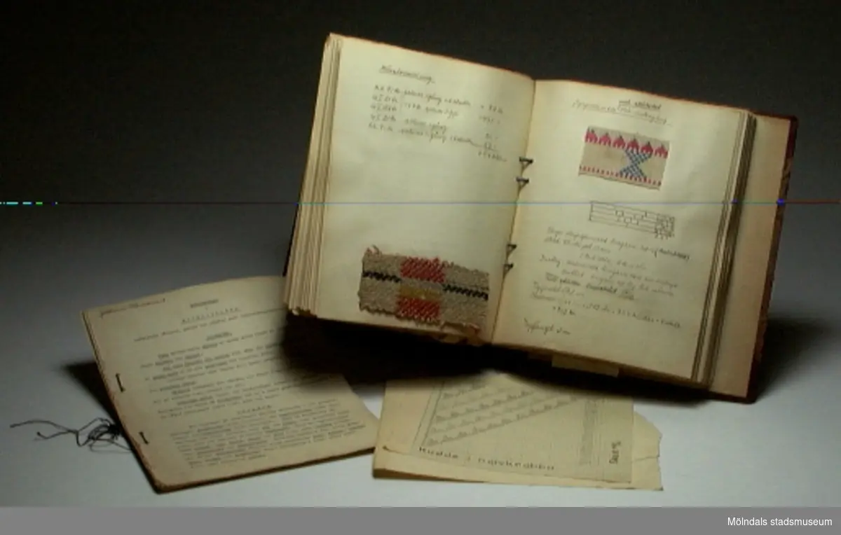 Pärm med titeln "Praktisk vävbok", med exempel på olika vävtekninker, som illustreras med textila vävexempel. Pärmen innehåller också ihopbundna pappersark med titeln "Anteckningar i materiallära", samt emellanåt lösa papperslappar.