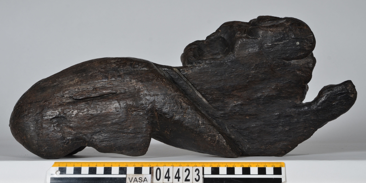 Skulptur av ett litet, liggande lejon med utsträckta framben och hopdragna bakben.
Lejonet är riktat mot vänster, sett från betraktaren. Det snett hållna huvudet återges i det närmaste i en face. Större delen av svansen saknas. Den befintliga delen av svansen avtecknar sig mot lejonets vänstra lår.

Lejonet är endast delvist rundskulpterat. På baksidan, i höjd med huvudet och höger framben, återfinns ett stort, snett urtag som bildar en slät anliggningsyta. Skulpturens framparti är således endast till hälften så tjockt som dess bakparti.
Bakkroppen är kraftigt sliten och skadad. Vänster bakben saknas, liksom större delen av svansen.

Text in English: Sculpture of a small reclining lion with its forelegs extended and its  hind legs tucked beneath its body.
Facing to the observer''s left, the head, held crookedly, is nearly en face. A large part of the tail is missing, and the remainder curves towards the left hind leg.

The lion is only partly three-dimensional. On the rear at the head height and at the right foreleg a large oblique hole forms a flat area for attachement, thus the forepart of the sculpture is thus only half as thick as its rear.
The rear of the body is badly worn and damaged. The left hind leg has been broken off.