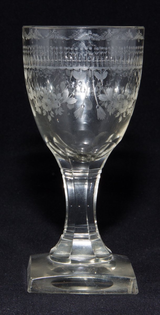 Sherryglas i empirestil från 1800-talets första hälft.
Med kvadratiskt slipad fot med fasetter samt med kulad botten. Åttpassformat och slipat ben med slipade ränder. Ovoidformad kuppa med slipad och graverad dekor kring kuppans mynning i form av en olivslipad bård och blomstergirlander med tofsar. Kuppan har en slipad ytterfasad kant.