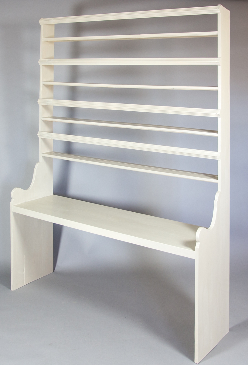 Hylla tillverkad av furu. Profilerade gavlar. Nedtill skiva och upptill fem hyllplan. Varje hyllplan har en profilerad list.