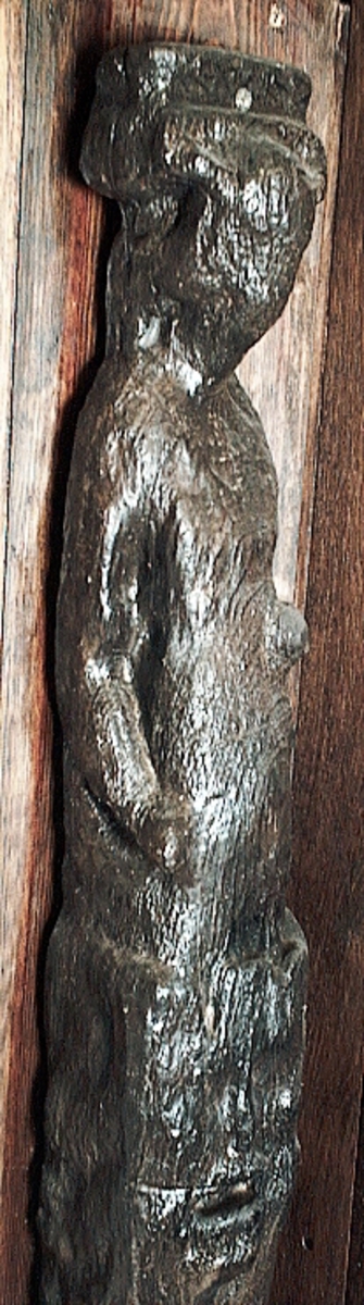 Skulpterad pilaster utformad som en karyatid med långt hår, troligen placerad under ett joniskt kapitäl.
Huvudet är vridet åt vänster. Höger arm är sträckt utefter sidan. Vänster arm är böjd och i handen håller figuren ett okänt föremål.
Pilasterskaftet är upptill prytt med en maskaron med bred, öppen mun och nedtill med en tung fruktfeston. Det nedåt avsmalnande pilasterskaftet avgränsas från piedestalen av en enkel vulst eller list med uppdragna kanter. Piedestalen är hög och jämnbred samt prydd med ett litet huvud och avslutas nedtill med en förtjockad bas. Skulpturens baksida är slät.
Skulpturen är kraftigt sliten och nött med finare detaljer utplånade.

Text in English: Sculpted pilaster with Caryatid with long hair under what is possibly an Ionic capital.
The head is turned to the left, the right arm is streched along the side, the left arm is bent and the hand holds an unknown object.
The shaft of the pilaster is decorated above with a mask with a broad, open mouth, below is a heavy festoon of fruit. The shaft tapers downwards and is divided from its pedestal by a simple torus or batten with drawn-up edges. The pedestal is high and even in width and decorated with a small head. It terminates at the bottom in a thickened base. Its back is smooth.
The sculpture is much worn, with finer details obliterated.