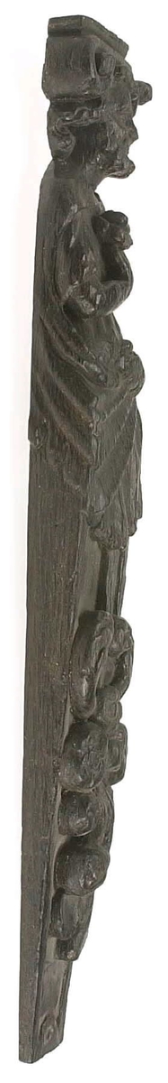Hermpilaster.
Liten skulpterad pilaster föreställande skäggig herm under joniskt kapitäl.
Huvudet är vridet mot vänster. Hermen är insvept i en mantel som hålls fast med vänster hand framför magen. I höger hand håller figuren ett okänt föremål (blomsterkälk?) framför bröstet. Pilasterskaftet är prytt med stora frukter och blad, fasthängande vid en stängel som delvis täcker det nedåt avsmalnande skaftets ramverk. Baksidan är slät.
Skulpturen är mycket välbevarad med sju spikhål.

Text in English: Small sculpted pilaster with a bearded Herm beneath an Ionic capital.
The head of the figure is turned to the left. The Herm is enveloped in a mantle, held fast with the left hand in front of its stomach. Its right hand holds an unknown object (a bunch of flowers?) in front of its breast. The shaft of the pilaster is decked with large fruit and leaves hanging from a stalk which partly cover the framing of the tapering shaft. Its back is flat.
The sculpture is very well preserved.