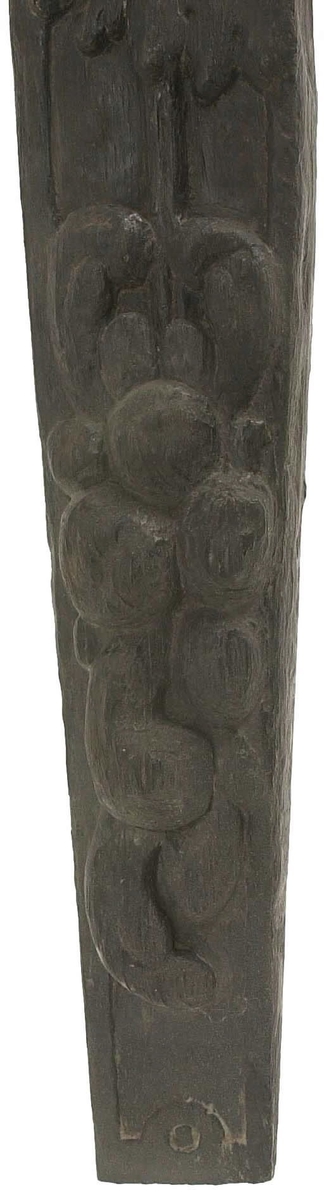 Hermpilaster.

Liten pilaster i form av en karyatid, med långt böljande hår under joniskt kapitäl.

Huvudet är vridet en aning åt höger. Med vänster hand hålls manteln samlad. I höger hand håller figuren en frukt eller dylikt framför bröstet. Pilasterskaftet är prytt med stora frukter och blad, fasthängande vid en stängel som delvis täcker det nedåt avsmalnande skaftets ramverk. Baksidan är slät.

Skulpturen är välbevarad, förutom ansiktet som är kraftigt slitet.

Fyra stycken spikhål, en övertäckt med en plugg.


Text in English: Sculpted small pilaster with a Caryatid with long wavy hair beneath an Ionic capital.

Its head is turned slightly to the right, its left hand holds its gathered mantle. Its right hand holds fruit or the like in front of its brests. The shaft of the pilaster is decorated with fruit and large leaves hanging from a stalk, which partly cover the framing of the tapering shaft. Its back is flat.

The sculpture is somewhat worn, its facial expression has been obliterated.