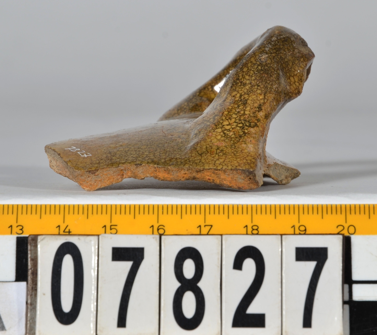 Del av skål.
1 st vertikal bandhänkel, tummad, 70 x 60 mm. Fragment av mynningsrand och buk. In- och utsida blyglaserad gulgrön.