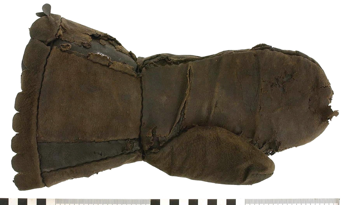 En kragvante till höger hand. Sydd av flera kraftiga läderstycken. Påsydd bård i ett stycke i form av rundade "tungor" längs kragkanten.