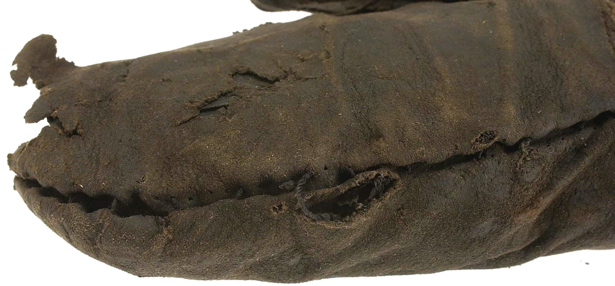 En kragvante till höger hand. Sydd av flera kraftiga läderstycken. Påsydd bård i ett stycke i form av rundade "tungor" längs kragkanten.