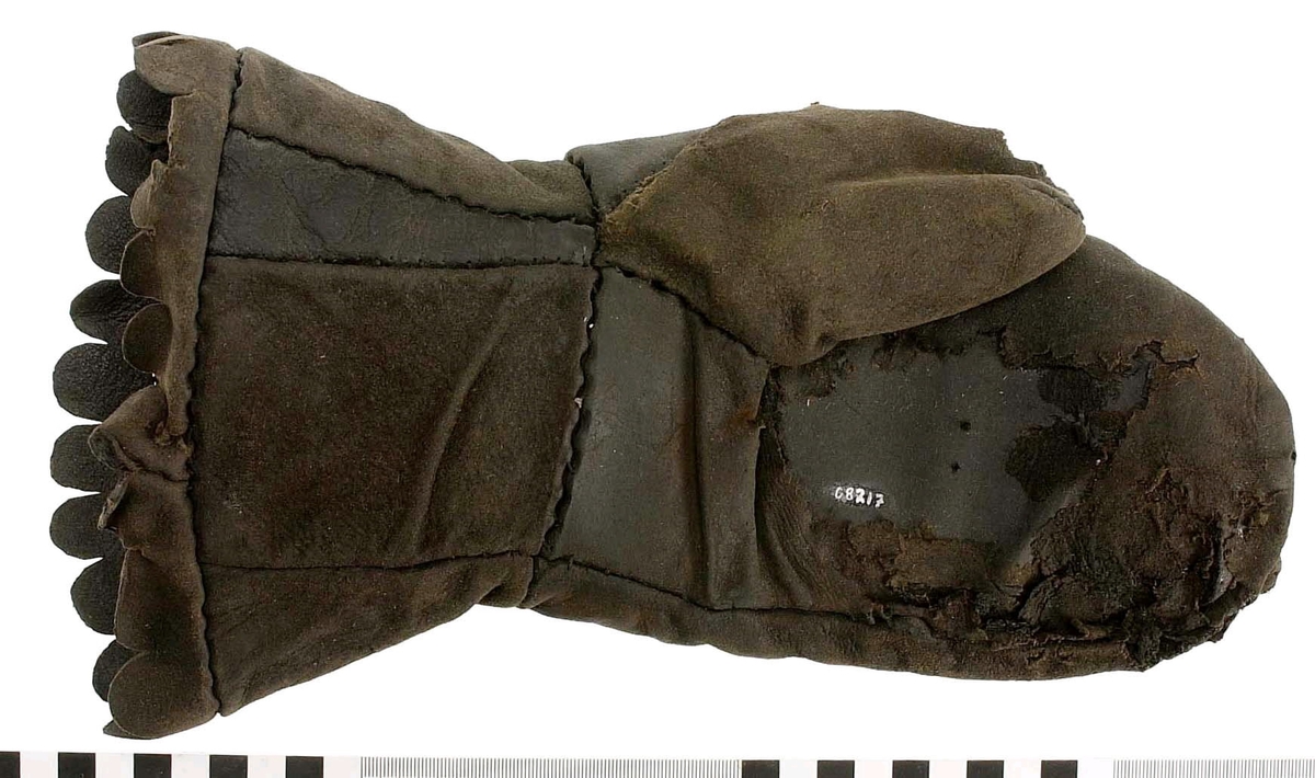 En kragvante till vänster hand. Sydd av flera kraftiga läderstycken. Påsydd bård i ett stycke i form av rundade "tungor" längs kragkanten.
