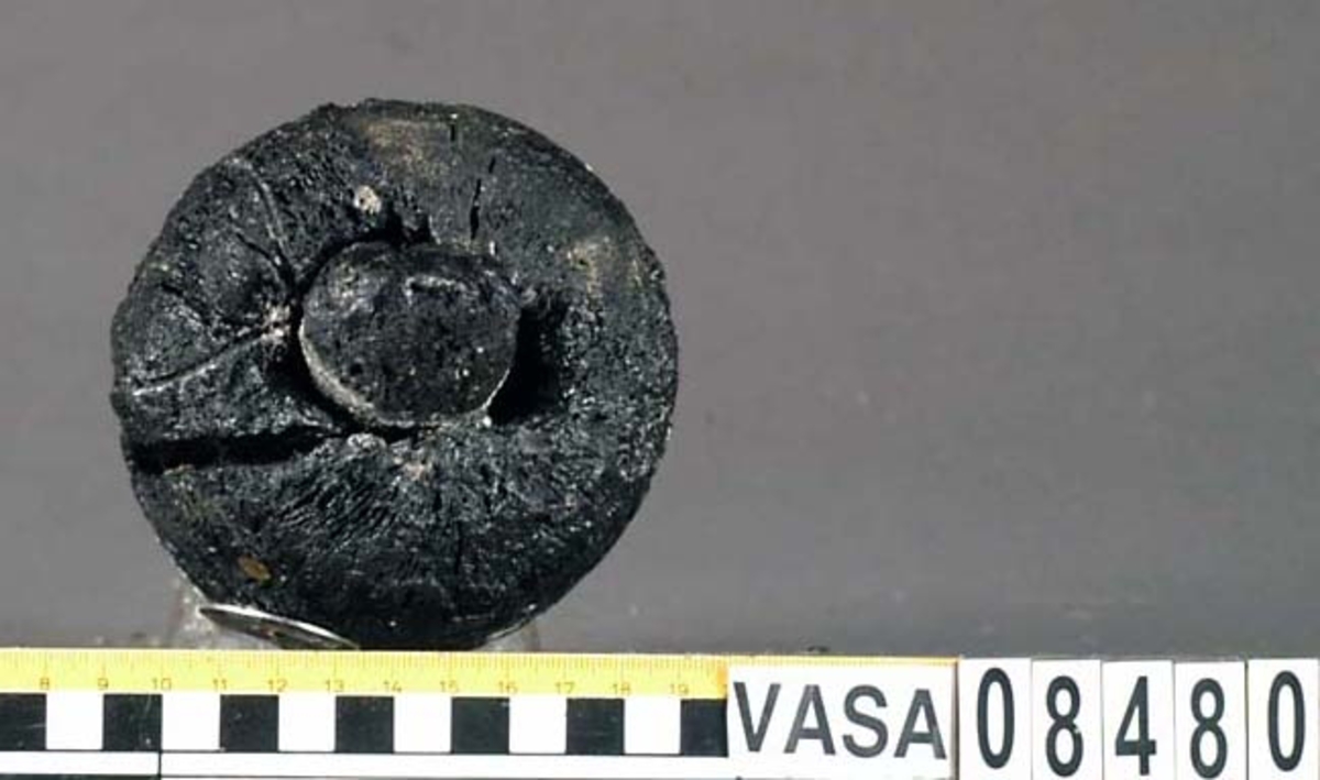 Kolv till viskare. Kolven består av ett cylindriskt svarvat trästycke med ett centrerat genomgående hål för skaftet. Den övre änden, åt skaftet till, har ursprungligen haft en utsparad fläns som idag är borteroderad. Kolven är kraftigt eroderad och sprucken. En del av skaftet sitter kvar.