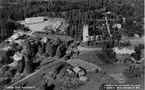 Vykort. Flygfoto över Anundgård. Skolan, byggd 1952, överst t v, kommunala lärarbostäder (bl a bodde läraren och kantorn Mauritz Öhnedal där). T v syns prästgården och i träddungen mitt emot lagården är nya affären. Huset nere t h är gamla skolan, nu (1987) församlingshem.