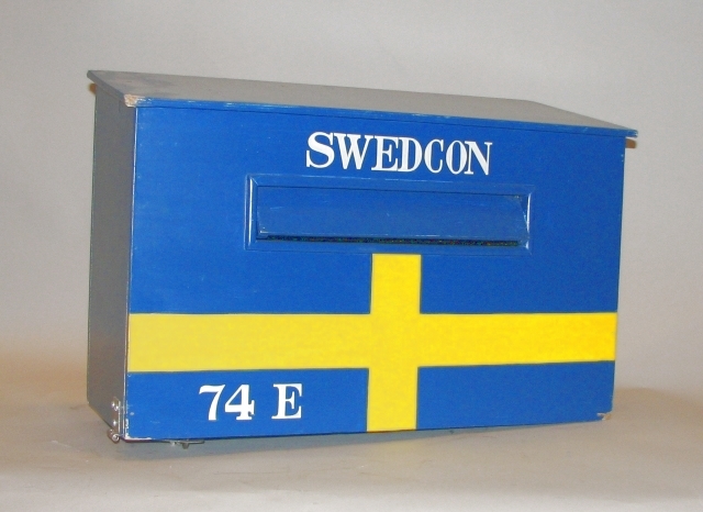 Brevlåda i trä med klaff för iläggsöppningen.
Iläggsöppningenhar mått:L=330 mm, H=40 mm. På fronten är lådan målad som den svenskaflaggan. Tömningslucka i botten, låsbar med hänglås.