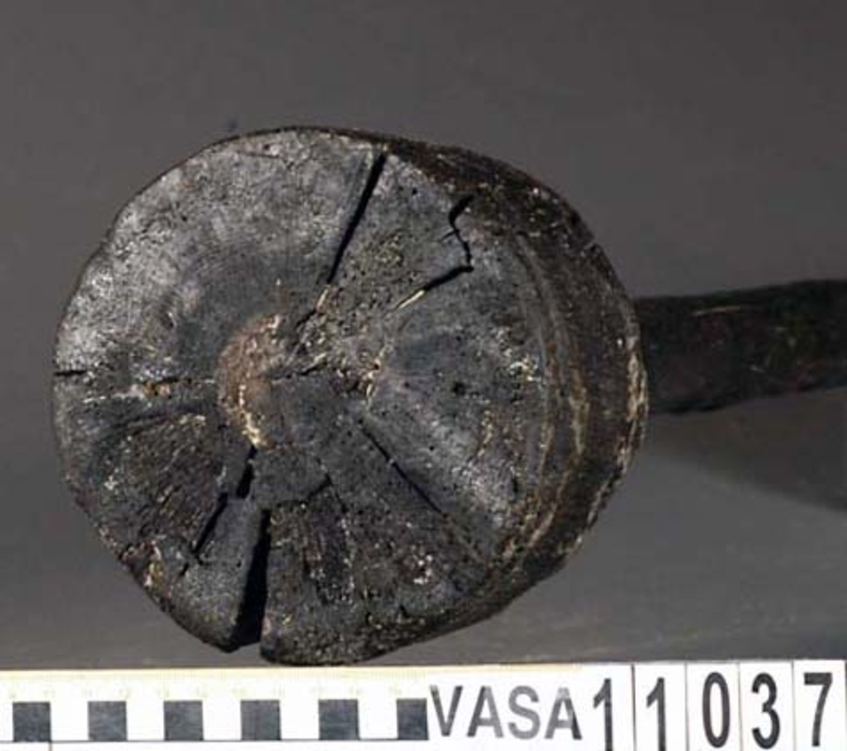 Kolv till ansättare. Kolven består av ett cylindriskt, svarvat, trästycke med ett centrerat skafthål. I övre änden, åt skaftet till, är kolven profilsvarvad. Motsatt ände är platt. Några sprickor, annars i fint skick.