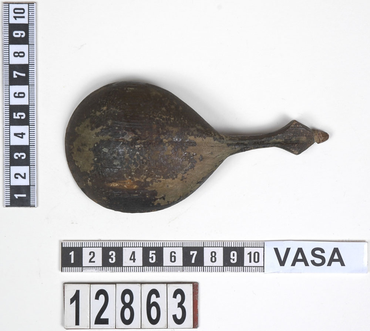 En träsked. Skeden har ett ovalt skedblad och ett kort skaft. Skaftets ände är rombformat samt försett med en liten knopp. På skedbladet syns en inristad dekor.

Skeden är välbevarad och har synliga färgspår.

För mer information se Dokumentationsblankett under Referenser – Länkade filer.