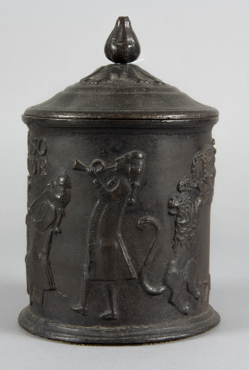 Relief på burken med text. Relief med rökande och spelande män. Några av männen sitter vid en spis. Riksvapen med flankerande lejon. Årtal 1794.
Text på burken. ORE FUMOSO BENE BIBENTUR.