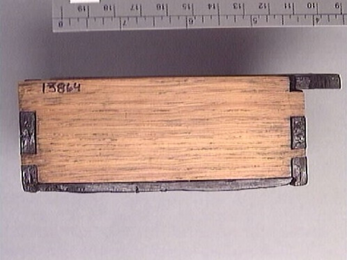 Ett litet träskrin med skjutlock.
Skrinets gavlar och långsidor är sinkade. Bottnen sitter infälld i gavlarna och är fästad med trästift vid långsidorna. Skrinet är försett med tre, löstagbara mellanväggar. På insidan av skrinet finns spår för mellanväggarna och för locket. Lockets ena ände är profilerad och har en liten halvcirkelformad urholkning som fungerar som tumgrepp. Den profilerade änden skjuter ut en bit utanför skrinet, då locket är stängt.
Två av skrinets mellanväggar samt en av långsidorna är rekonstruerade. Längs med skrinets ena långsidan löper en spricka. Skrinet är i gott skick.