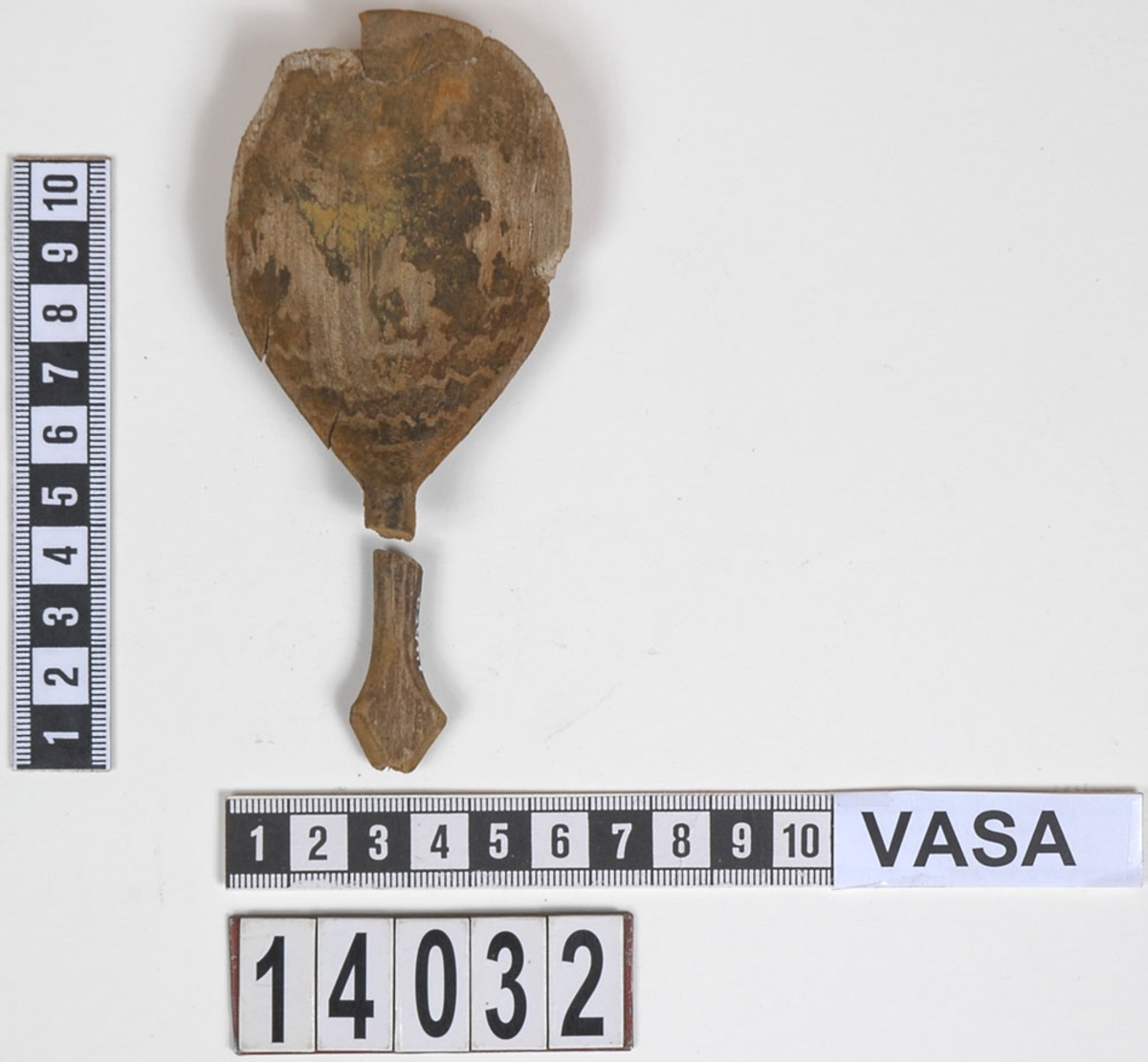 Fyra delar av en träsked. De två större delarna utgör skedskaftet samt större del av skedbladet med ett mindre parti av skaftet. De övriga två delarna utgör fragment av skedblad.

Insidan av skedbladet är dekorerad med ett ristat/glödritat vågmönster. Skedskaftet är kort och rakt, med profilerad skaftände. Längst ut på skaftänden syns en brottyta. Troligtvis har skaftet avlutats i en ändknopp. Skeden har gul-röda utfällningar samt rödbruna färgspår.

Skeddelarna är mycket ömtåliga, med sprickor.

För mer information se Dokumentationsblankett under Referenser – Länkade filer.