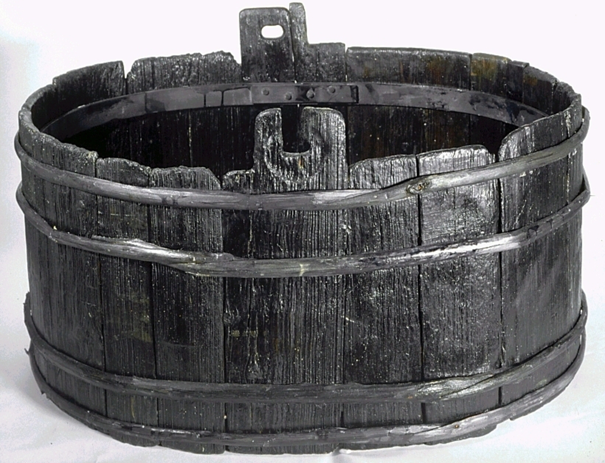 Laggstav till en balja. I stavens övre del finns ett urtag för en regel eller tvärslå. Urtaget är skadat och den övre delen saknas. Runt urtaget finns en fasad nedsänkning, eventuellt för någon form av beslag. På insidan av stavens nedre ände finns ett urtag. Urtaget är ett hugget spår där baljans bottenplatta sitter.