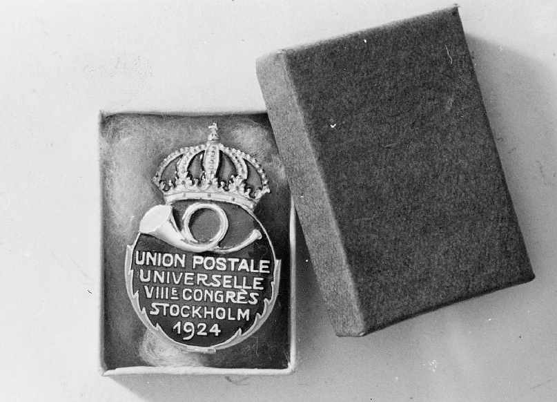 Deltagarmärke för delegaterna vid VIII Världspostkongressen i
Stockholm 1924.Posthorn i guld på blå guldkransad emaljerad sköld.
Däröver krona i guld och rött.