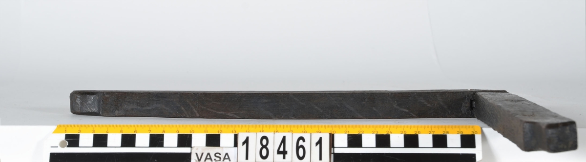 En vinkelhake.

Vinkelhaken består av två plana stavar som är sammanfogade genom sinkning. Ändarna är profilerade. I mitten av den kortare staven finns ett runt hål för upphängning.

Vinkelhaken är välbevarad och i gott skick.

För mer information se Dokumentationsblankett under Referenser – Länkade filer.