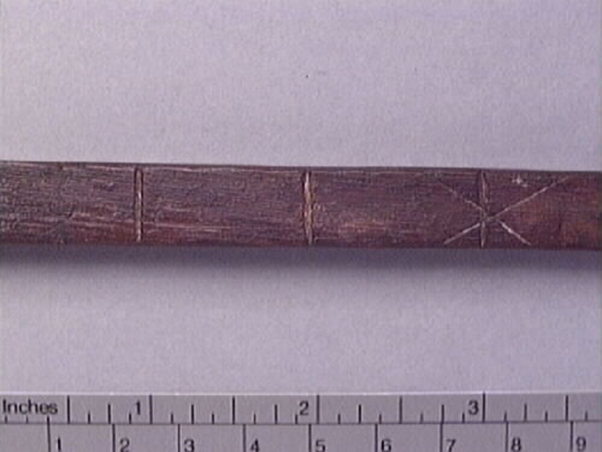 En tumstock av trä.

Tumstocken är försedd med elva inristade skåror som markerar tolv tum. På den mittersta skåran finns ett inristat kryss. Ytterligare ett kryss, dock något mindre, har ristats in vid skåran närmast mittskåran.

Tumstocken är i gott skick.

För mer information se Dokumentationsblankett under Referenser – Länkade filer.