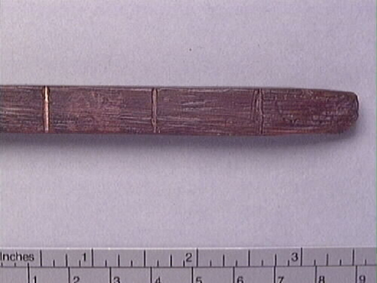 En tumstock av trä.

Tumstocken är försedd med elva inristade skåror som markerar tolv tum. På den mittersta skåran finns ett inristat kryss. Ytterligare ett kryss, dock något mindre, har ristats in vid skåran närmast mittskåran.

Tumstocken är i gott skick.

För mer information se Dokumentationsblankett under Referenser – Länkade filer.