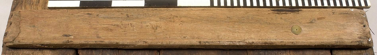 Tvärslå till däckslucka.
Fasad i båda ändarna. Tre genomgående hål i ena änden, ett i det andra.
Fäst vid fem brädor med ca 30 skruvar.