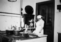 Hilma Olsson arbetar i köket och mäter upp något på en våg i