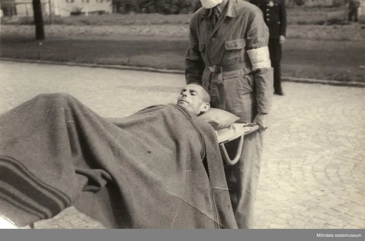 "Karantänsförläggning" på Kvarnbyskolan för överlevande från koncentrationsläger i Tyskland och Polen 1945.  
Skolan fungerade under denna sommar som beredsskapssjukhus.

Manlig flykting på bår, buren av Röda Korsets personal.