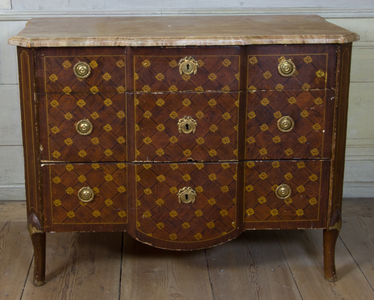 Byrå av furu, med imitationsmåleri som efterliknar fanér och inläggningar i olika träslag, i form av rutinläggningar och blommor. Med marmorerad skiva av trä. Rak form med avfasade hörn, med svagt svängda ben. Fronten med förkroppat mittparti, som nedåt avslutas i svagt bågformat undergehäng. Med tre lådor med nyckelbrickor med bandrosetter och beslag med dragringar i form av lagerkransar av förgylld mässing.