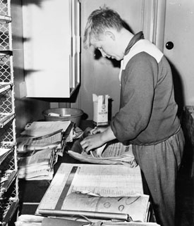 Brevbärarebiträdet Anders Håkansson fördelar postabonnerade tidningar efter utdelningslista.  Postexpeditionen i Åkersberga, augusti 1961.