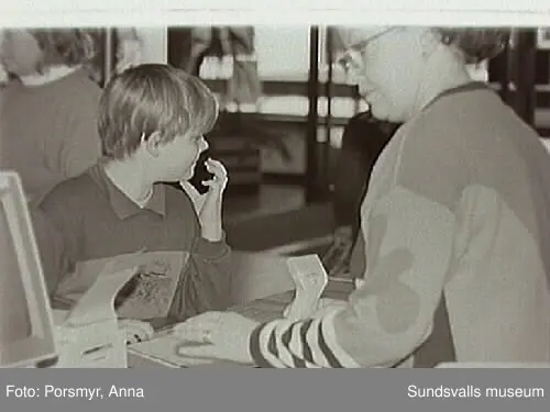 Dokumentationsfotografering av verksamheten vid biblioteksfilialen i Matfors. Bild 01Biblioteksassistenten Ingrid Engström, Matfors bibliotek, med låntagare vid utlånedisken. Bild 09 bibliotekaren Inger Barkman läser för en grupp förskolebarn i bibliotekets "läsrum".