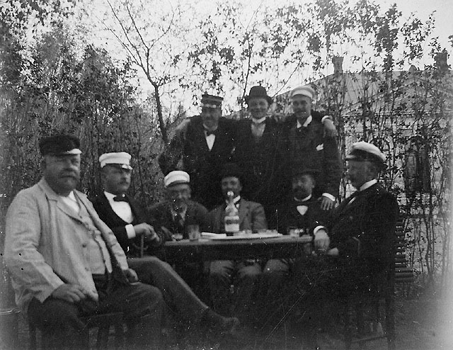 Nio medlemmar i Storviks postklubb fotograferade i
Överliggningslokalens trädgård i Storvik, juni 1900. Sittande från
vänster: Fanjunkaren, Kalle P-s, Jockus, Pliggen, Magnus, Carl
Kihlberg. Stående från vänster: "Gasqueu", Axel, Blombergsson.