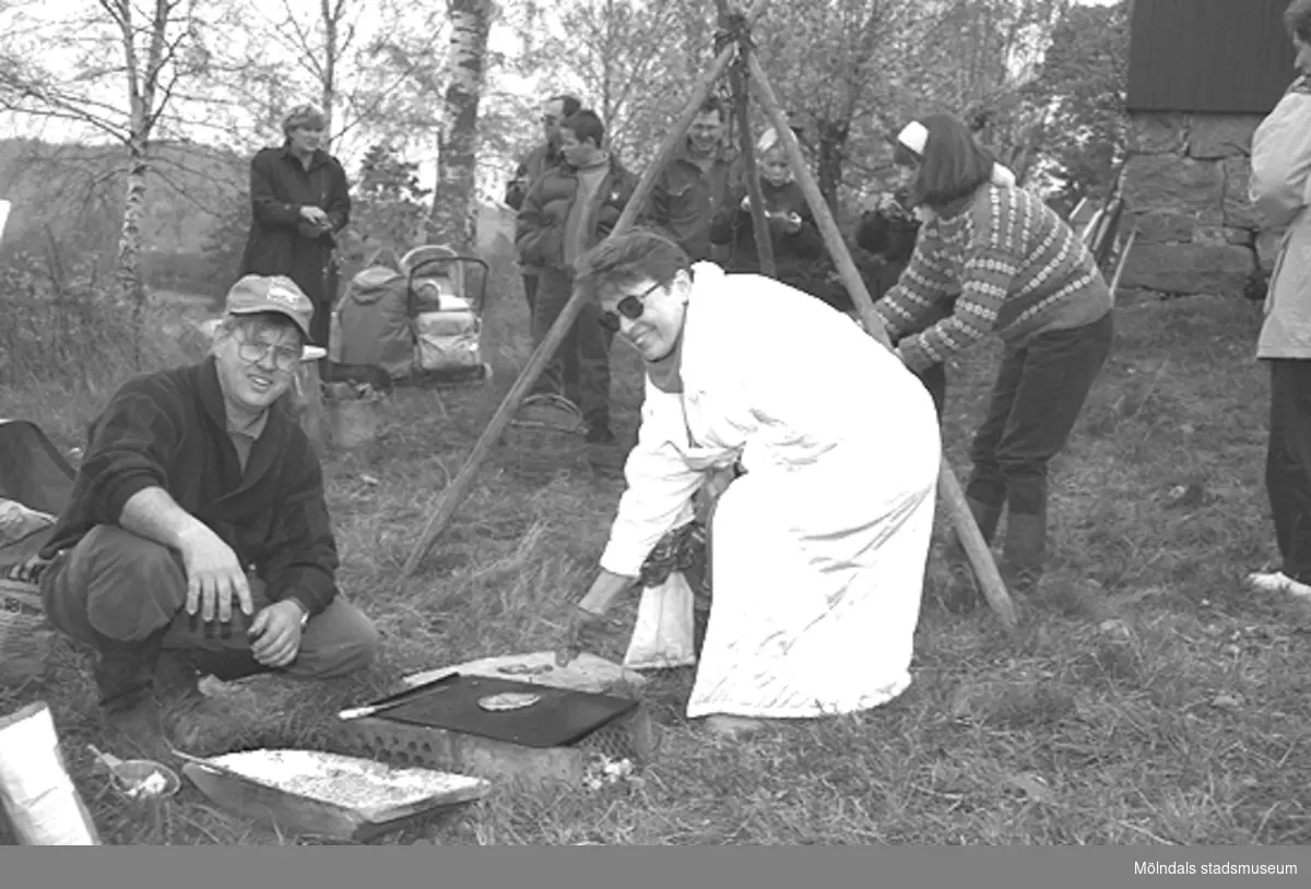 Familjesöndag vid Börjesgården, 1994-05-15. Museitekniker Alf Garthman sitter på huk och grillar. Museichef Mari-Louise Olsson kokar mat över öppen eld.