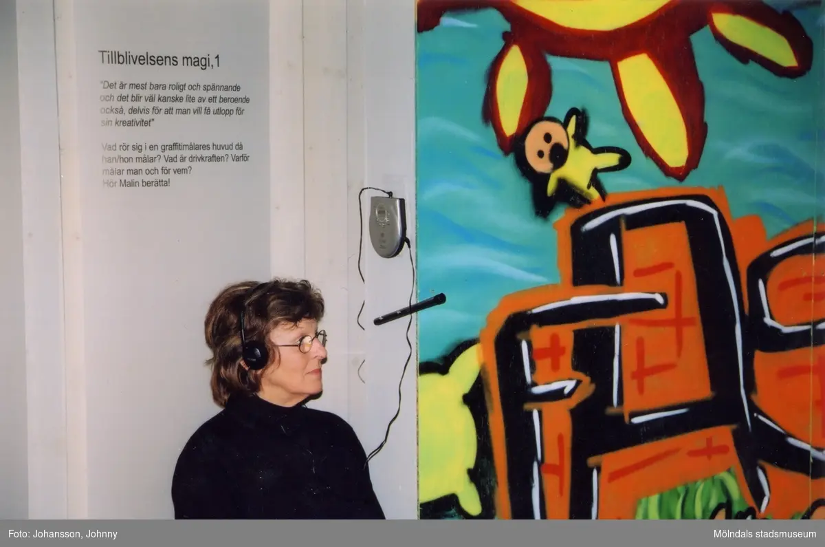 Birgitta Johansson lyssnar med hörlurar i utställningen "Alltså finns jag" på Mölndals museum, år 2003.

Från utställningen "Alltså finns jag" som handlade om graffitikultur. Pågick 25 januari - 25 maj 2003 på Mölndals Museum (senare Mölndals stadsmuseum). Produktionen var ett samarbete mellan Mölndals Museum, Vitlycke museum, Bohusläns museum, Västergötlands museum och Konstkonsulenterna i Västra Götalandsregionen.