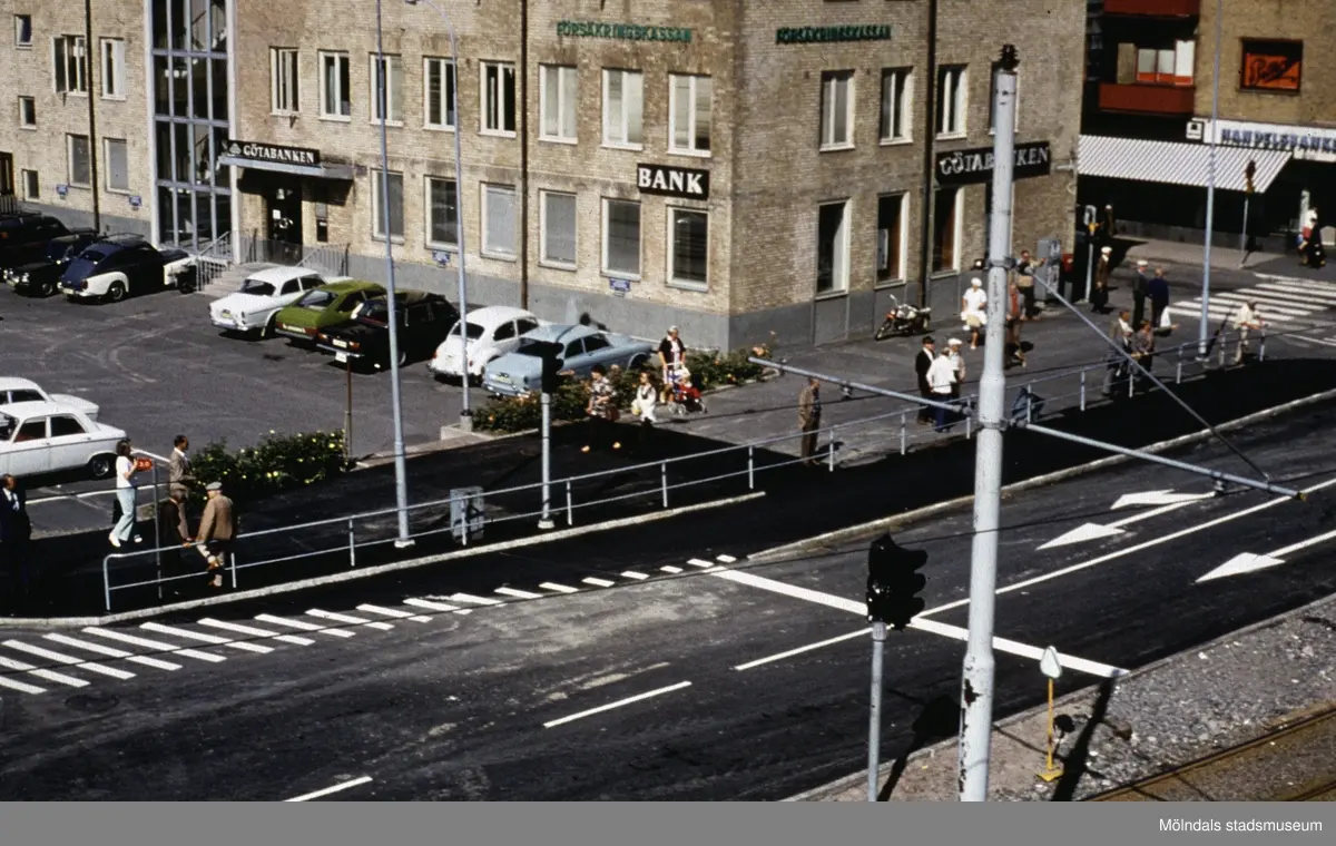 Vy från Mölndals Bro ner mot parkerade bilar på Broplatsen, Hantverkshuset och Kungsbackavägen i Mölndal, 1970-tal. Till höger ses början av Frölundagatan.