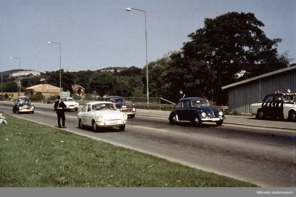 Poliskontroll på Kungsbackavägen i Mölndal, då vi fortfarande hade vänstertrafik, cirka 1965 - 1966. Högertrafik infördes september 1967. I bakgrunden ses Störtfjället och lägenheter på Delbanco- och Lövgatan.