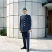 Brevbärare fotograferad utomhus i 1962 års vinteruniform. Uniformen är av gråblått ylletyg; enradig kavaj med fyra stora uniformsknappar, fyra fickor med lock. Bröstfickans lock knäpps med uniformsknapp av mellanstor storlek. Byxor utan slag och båtmössa försedd med mössmärke med en vinkel vilket var avsett för postiljoner och expeditionsvakter.