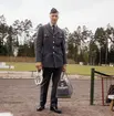Brevbärare i uniform modell 1962, fotograferad på en idrottsplats med spikskor i höger hand och en väska i vänster.