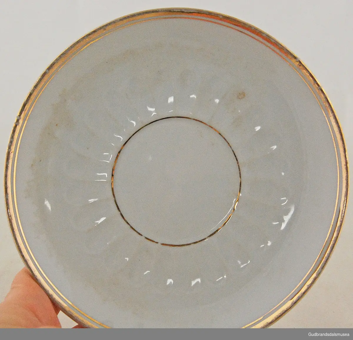 Hvit skål med gullkant øverst og ring av gull på midten av skålen, på midten er også lette, avlange fordypninger.  