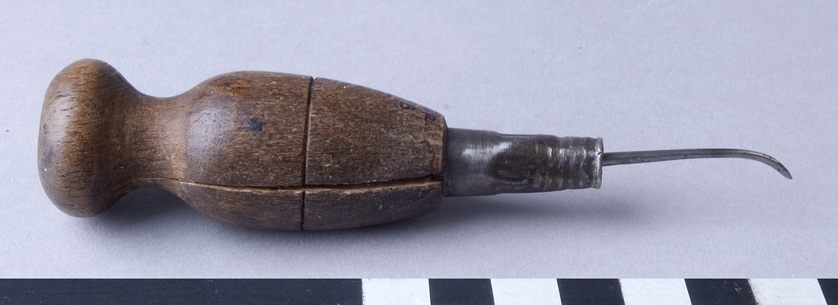Syl, tvärsyl, med syl av stål med svarvat handtag av trä. Sylen är fäst i handtaget med hjälp av en metallhylsa och är böjd med slipat kantstående skär. Handtaget har en genomgående spricka samt ett utskuret kryss i änden.
Sylen har en fabriksstämpel som delvis döljs av förstärkningen, endast "..SON" är synligt.