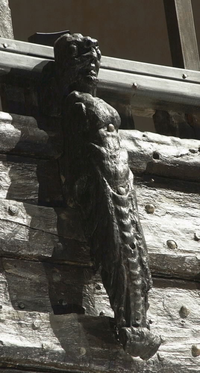 Skulptur i form av en slätrakad herm med öppen mun och stor, bred näsa.
På hjässan sitter ett djurhuvud troligtvis föreställande ett lejon. Armar är ersatta av upprullade bladslingor. Hermens nederdel är formad till ett fodralliknande "hölje" prytt med bladslingor. Ornamentiken är av organisk karaktär med större och mindre, elegant formade bladslingor. Nedtill är "höljet" upprullat till en vulst. Sedd från sidan är hermen avsmalnande nedtill.
Baksidan, som har utgjort anliggningsyta, är försedd med ett antal stora urtag i höjd med hermens hjässa, bröstparti samt från midjan och nedåt. I midjehöjd återfinns även ett högsmalt urtag utmed baksidans ena hälft. Strax nedanför midjan går sidledes ett stort hål tvärs igenom skulpturen.
Skulpturen är delvis kraftigt sliten och finare detaljer i utförande har därför gått förlorade.

Text in English: Sculpture in the form of a clean-shaven Herm with open mouth and large, broad nose.
On top of his head is the head of an animal, possibly a lion. The arms have been replaced by strands of rolled-up leaves. The lower part of the Herm is sheathed in a "cover", decorated with leaf strands. The bottom of the "cover" is rolled up into a torus. Its ornamentation is of a pronounced organic character, with larger and smaller chains or festoons of leaves. Seen in profile, the Herm tapers downwards.
The back, also the attachment surface, has a number of large cut-out holes on the same level as the Herm''s head, chest, waist and further down. At one side of the back of the waist there is also a narrow vertical groove. Just below the waist, a large hole passes through the Herm.
The sculpture is very worn in places and any finer details have been lost.