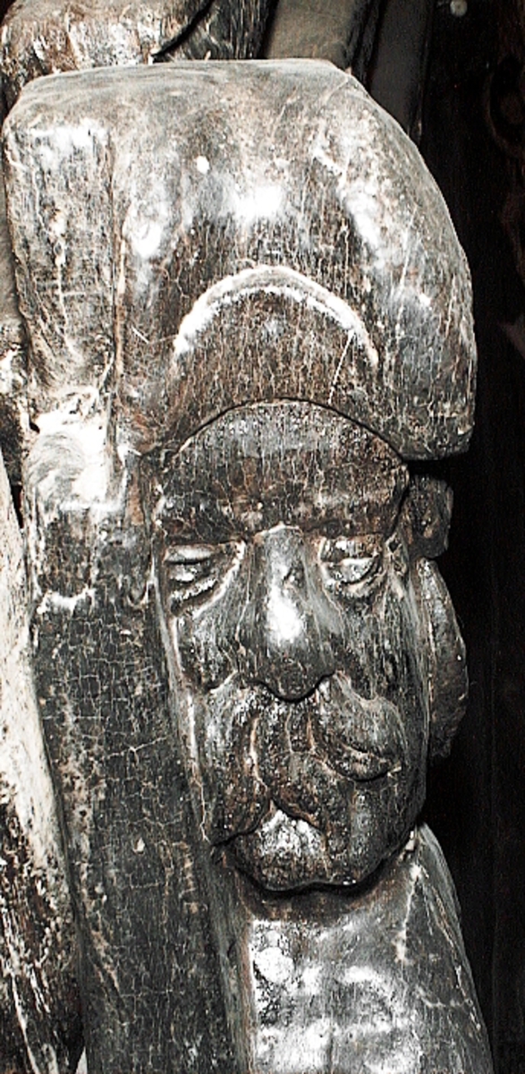 Skulptur av en triton, svängd mot höger.
Tritonen är framställd i vänster profil och avtecknar sig i hög relief mot det släta bakstycket. Tritonen har en stor näsa och treflikig mustasch. På huvudet sitter en hjälm med dekorativa bladvoluter. Armarna är ersatta av långa, flikiga bladslingor. Bålens övergång i den fjällförsedda fiskstjärten markeras av stora bladbildningar. Tritonens stjärt döljs bakom stjärten och vingen till en under liggande drake, se fyndnummer 21277. På baksidan finns urtag för relingslisten.
Skulpturen är mycket välbevarad.

Text in English: A sculpture of a Triton curved to the right.
The figure is seen in left profile, in high relief against a plain back board. The face has a large nose and a moustache that splits into three parts. On its head is a helmet with decorative leaf volutes. The arms are replaced by long, lobed leaf formations. The transition area between the male torso and the scaled fish-tail is decorated with large leaves. The rear is hidden behind a dragon''s coiled tail and broad wing situated below, see No. 21277. There are notches on the back that fit into the railing.
The sculpture is very well preserved.