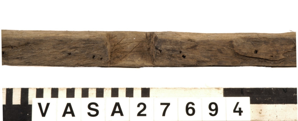 Relingslist. Den ena kortänden är uppfläkt. Den andra kortänden avslutas med en snedfasning, sannolikt en lask. Den andra slutar tvärt i sambands med en ursparning (sannolikt platsen för en årtull). Tolv stycken ej genomgående spikar i vad som sannolikt är den sida som vetter mot bordläggningen indikerar att den har spikats fast utifrån. Ett kraftigt genomgående hål syns i anslutning till ursparningarna för årtullarna. Spikhål syns i dessa avtrycks hörnor. På den sidan som vänder mot bordsidan och på undersidan syns snedfasade urtag, sannolikt för topparna till intimmer. I dessa urtagningar kan man skönja tydliga verktygsspår.