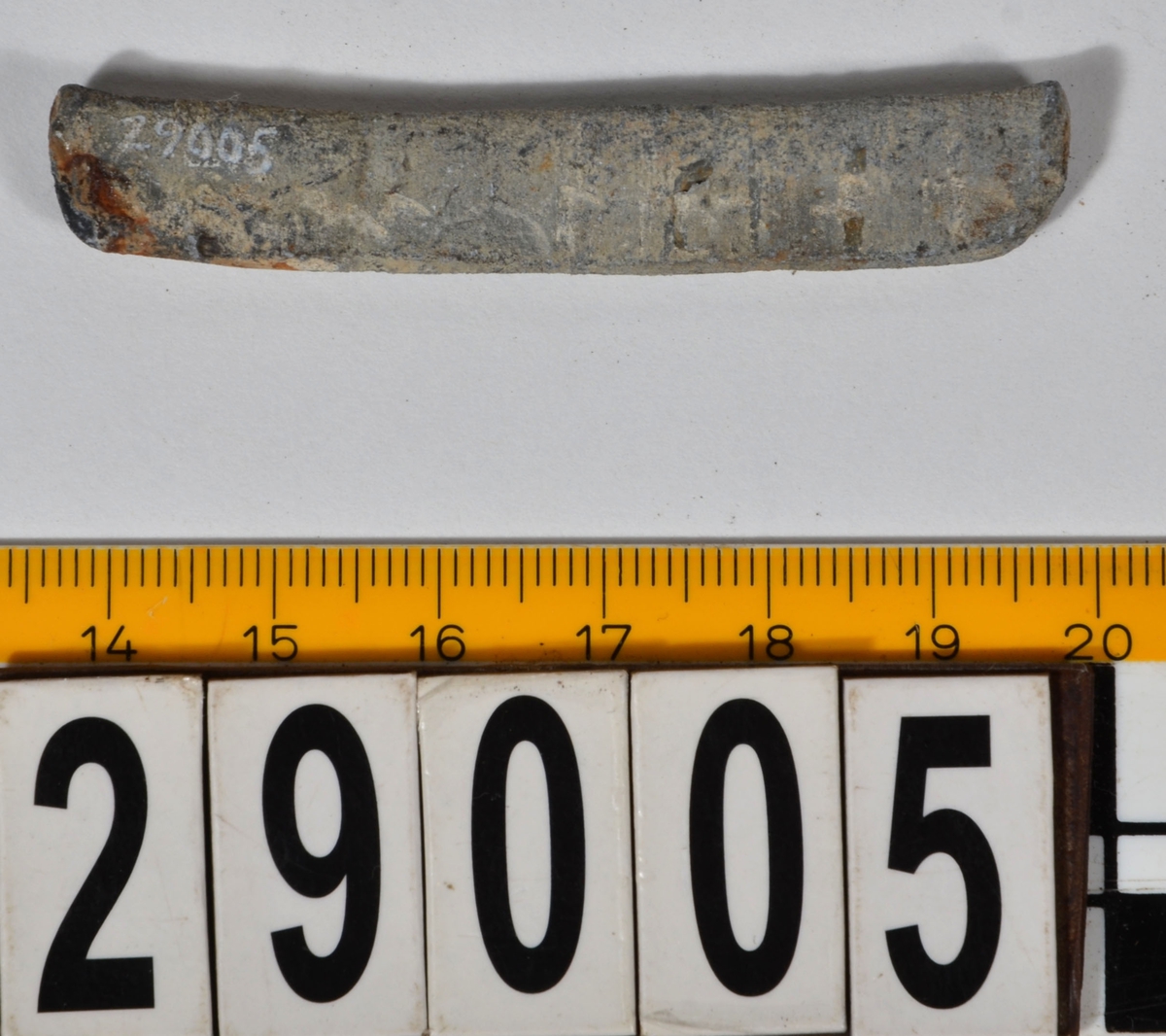 Sänket består av en vikt blybit. Sänket har tydliga märken efter det verktyg som pressat ihop sänket runt garntråden. Sänket är i gott skick.

Text in English: Lead sinker in the shape of a flat tube. The rectangular piece of lead is folded vertically in half and has visible tool marks from the folding process. The yarn is pushed through the hole. Grey mat in colour. In good condition.