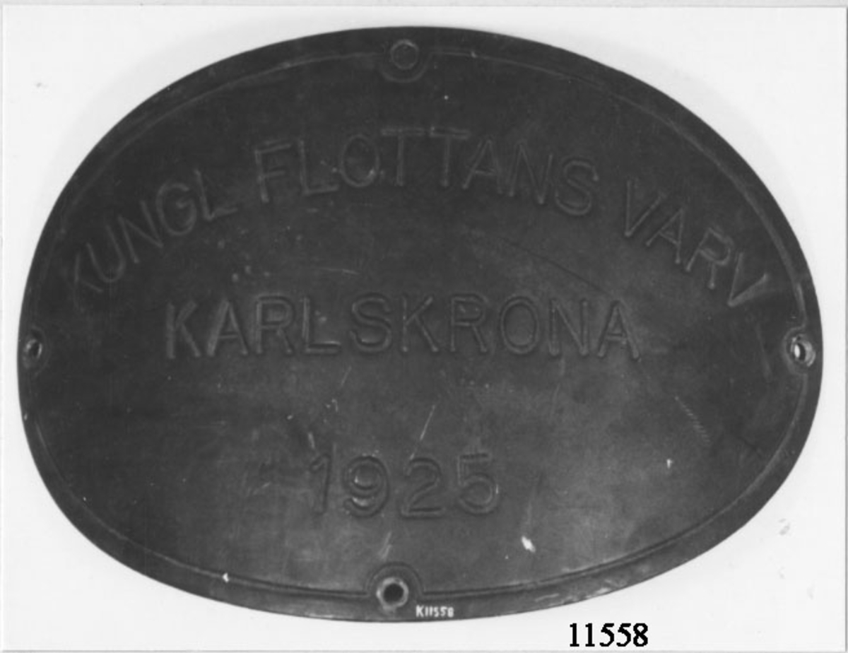 Försedd med texten Kungl Flottans Varv Karlskrona 1925.
Oval, något böjd och försedd med fyra hål för fastsättning.
Skylten har suttit på ubåten Valen. (Fartyget byggt på Karlskrona örlogsvarv år 1925, det skrotades 1949)