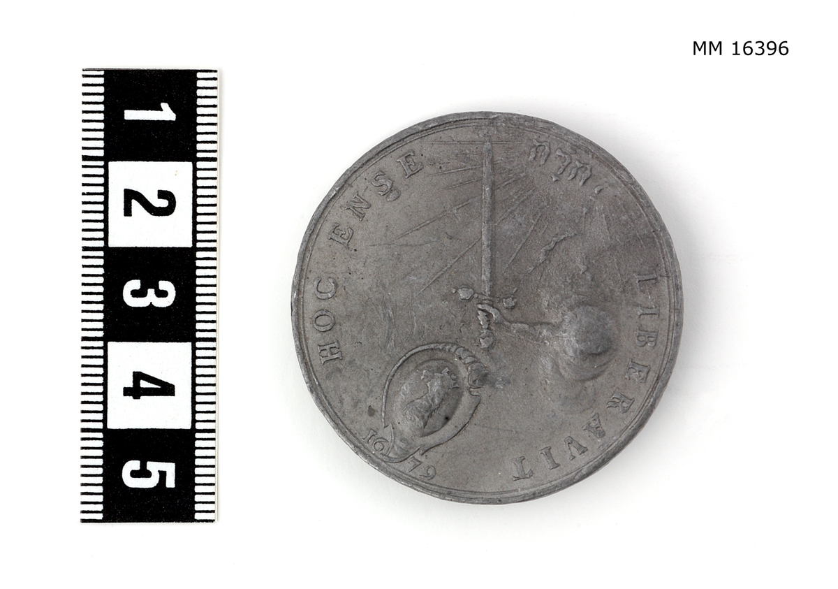 Cylindrisk medalj av tenn. Åtsidan: CAROLVS XI D: G. REX SVECIAE. Bröstbilden, höger sida, lagerkransad, i rika, brämade mantelveck uppfästade över axeln genom ett rutformigt smycke, halsen bar. Nedanför, nästan osynligt: AE. Frånsida: HOC ENSE. LIBERA VIT. En hand ur skyn håller ett svärd, vars fästeknapp och parerstång är prydda med tre kronor (otydliga) och på klingans början vid fästet konung Carl XI namnchiffer (nästan osynligt), över Skånes vapensköld (ett krönt griphuvud). Under skölden 1679. Överst ett strålande JEHOVA (hebreiska).