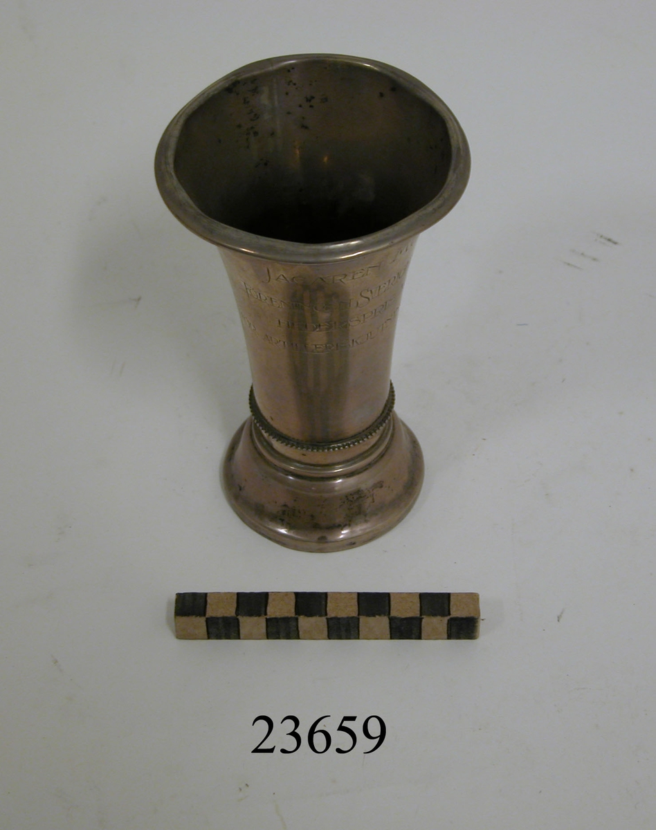 Pokal av silver. Konad, något insvängd med textad inskription "JAGAREN MUNIN. FÖRENINGEN SVERIGES FLOTTAS HEDERSPRISS 1915 FÖR ARTILLERISKJUTNING Å JAGARE". I botten silverstämpel samt "7, K. ANDERSSON".