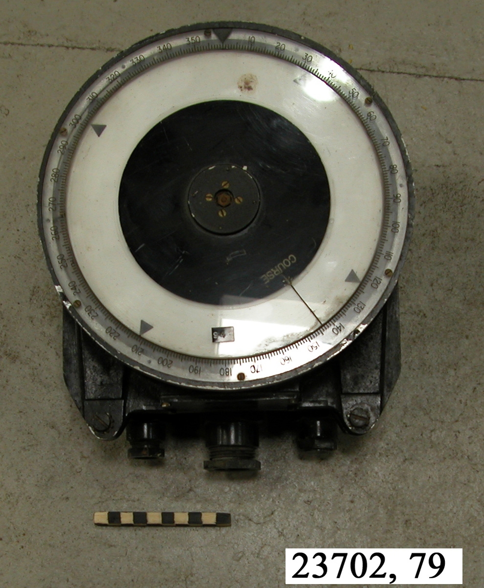 Svartlackerat kurs- och bäringsinstrument delbar i två delar vilka sitter ihop med fyra bultar. På nederdelens ena sida sitter tre kabelanslutningsöppningar. Instrumentets cirkulära ovansida är graderad i 360 grader och har en mekaniskt vridbar skiva av plast försedd med vit bakgrund. Skivan har en riktningspil försedd med texten "COURSE". Svarta pilar markerar var nittionde grad. Till instrumentet hör ett lock av metall.